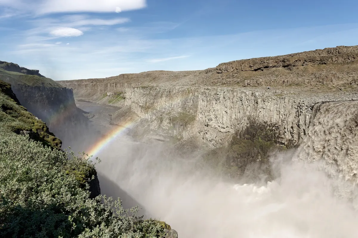 Der Dettifoss stürzt im Norden Islands in seine Schlucht, in der Gischt steht ein Regenbogen