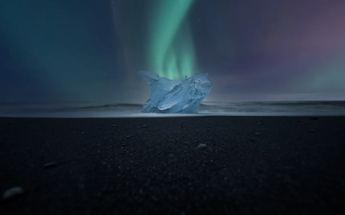 Polarlichter über einem Block Gletschereis am schwarzen Sandstrand Diamond Beach nahe der Gletscherlagune Jökulsárlón