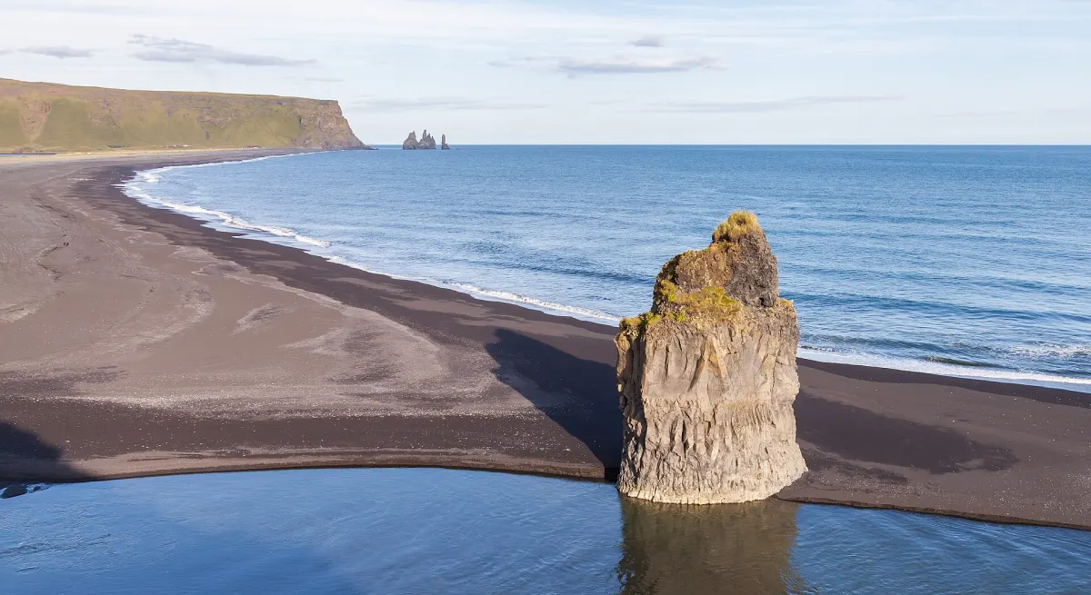 Basaltfelsen am schwarzen Sandstrand Reynisfjara bei Vík, im Hintergrund die Felsnadeln Reynisdrangar