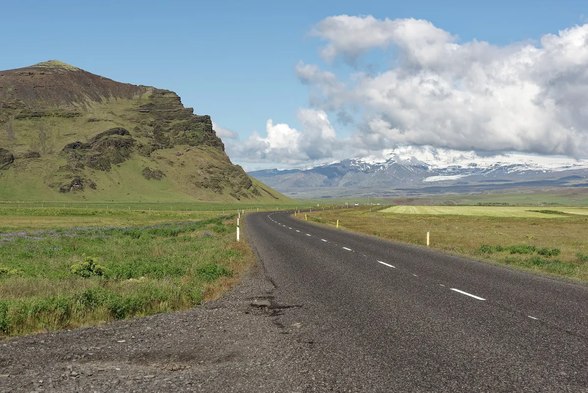 Die Ringstraße (Route 1) führt durch grünes Weideland im Süden Islands, im Hintergrund der Gletscher Mýrdalsjökull