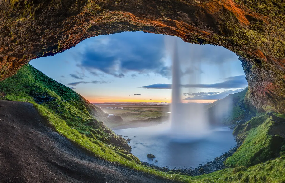Blick vom Pfad hinter dem Seljalandsfoss durch den fallenden Wasservorhang in den Sonnenuntergang