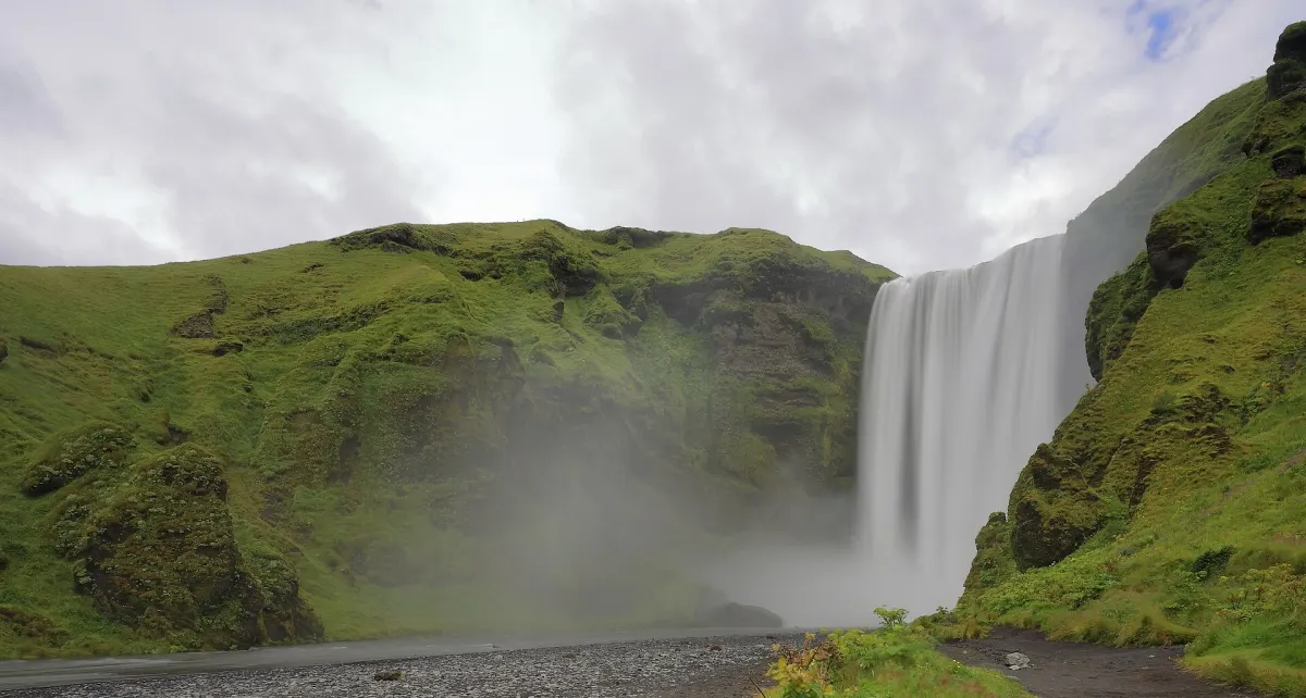 Der Skógafoss, seine Gischt zieht über die grünen Hänge neben dem Wasserfall